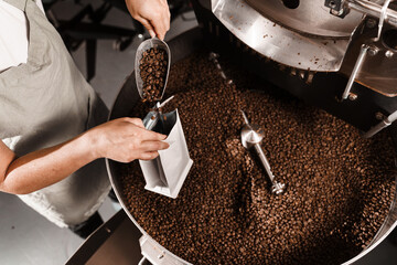 Filling coffee grains in a craft bag. Packing fried coffee beans. Worker pouring roasted coffee beans in packaging bag.