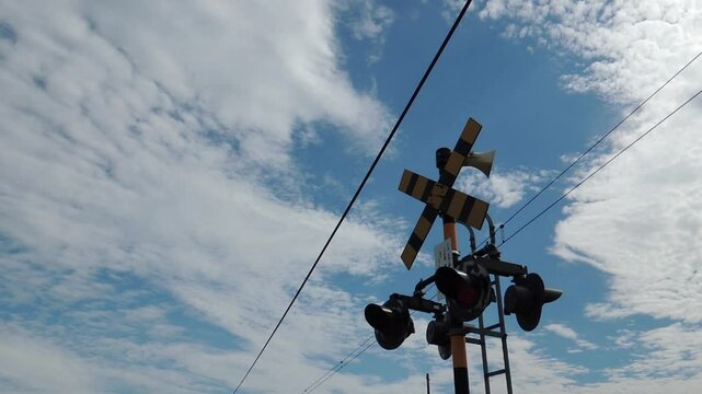 Japanese railway crossing signal flashing and train passing by / 雲が浮かぶ青空を背景に点滅する踏切と通過する電車