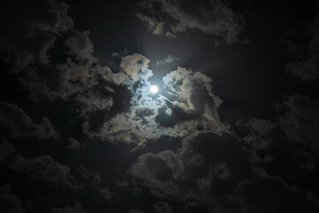 An image of the moon in a cloudy sky with scattered clouds that shows the moonlight beautifully