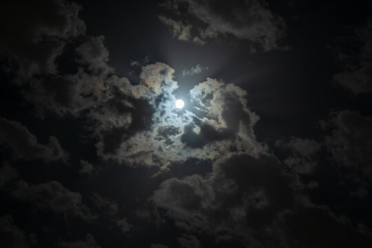 An image of the moon in a cloudy sky with scattered clouds that shows the moonlight beautifully