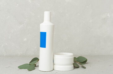Shampoo and hair mask with green leaves on concrete background