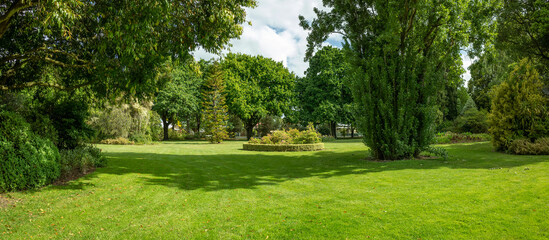 Panoramic background texture of a landscaped green outdoor space with expansive vacant recreational ground. Large grass lawn with mature trees. Colac Botanic Gardens, Australia.