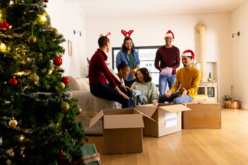 Young multiracial friends packing donations at home, celebrating Christmas together joyfully