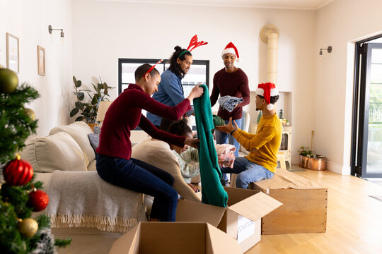 Christmas time, wearing festive hats, multiracial friends packing gifts in living room, at home - Powered by Adobe
