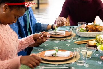 Christmas time, young multiracial friends holding hands around festive table, at home