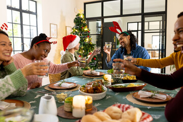 Celebrating Christmas, multiracial friends toasting drinks around festive table at home