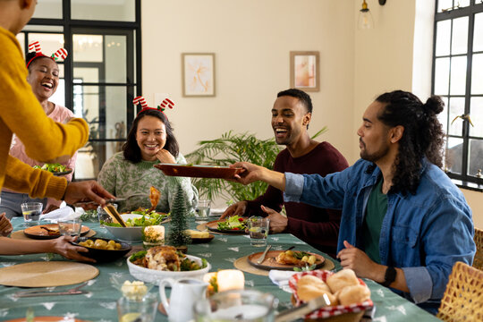 Christmas time, young multiracial friends enjoying festive holiday meal together, at home - Powered by Adobe
