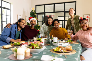 multiracial friends celebrating Christmas together, enjoying festive meal and holiday cheer, at home