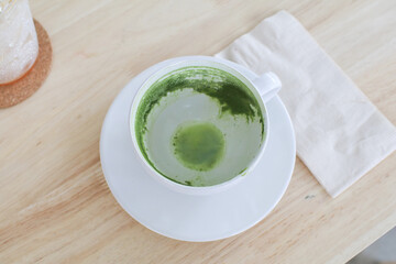Empty white cup of matcha green tea on wooden table. Dirty after drink in cafe or coffee shop..