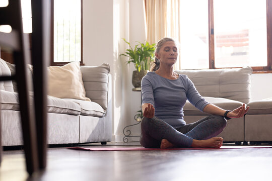 senior woman meditating on yoga mat at home, finding inner peace