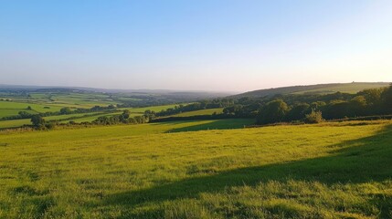 Fototapeta premium Scenic countryside landscape with green fields under a clear blue sky.