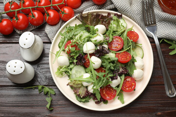 Tasty salad with arugula, lettuce, mozzarella cheese, vegetables and fork on wooden table, flat lay