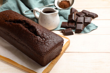 Tasty chocolate sponge cake and ingredients on white wooden table, closeup