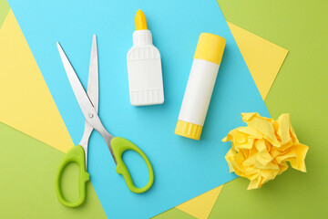 Different types of glue, colorful paper and scissors on green background, flat lay