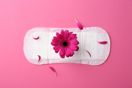 Menstrual pad with flower on pink background, top view