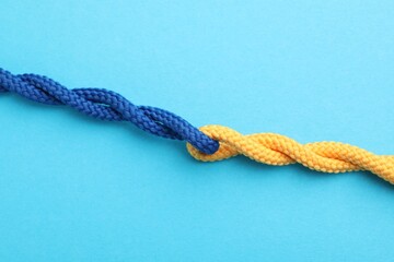 Colorful ropes tied together on light blue background, top view. Unity concept