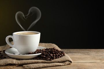 Fresh aromatic coffee and beans on wooden table, space for text. Steam in shape of heart over cup