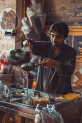 Pakistani street vendor pouring chai tea into cups in his roadside tea stall