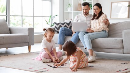 Happy sisters playing while their parents with laptop sitting on sofa at home