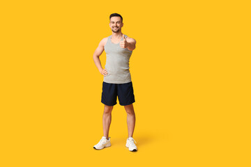 Handsome sporty young man showing thumb-up gesture on yellow background. Weight loss concept
