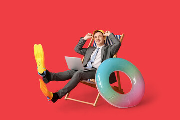 Office worker with inflatable ring and flippers sitting on deck chair with laptop on red background © Pixel-Shot