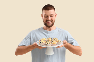 Young man with tasty muffins on beige background