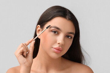 Fototapeta premium Young woman correcting shape of her eyebrows on grey background