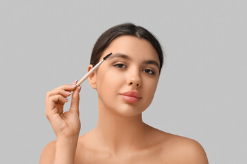 Fototapeta premium Young woman correcting shape of her eyebrows on grey background