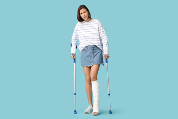 Young woman with broken leg and crutches on blue background