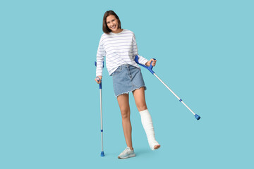 Young woman with broken leg and crutches on blue background