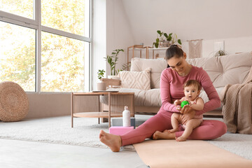 Fototapeta premium Sporty young mother with her little baby and massage ball sitting on mat at home