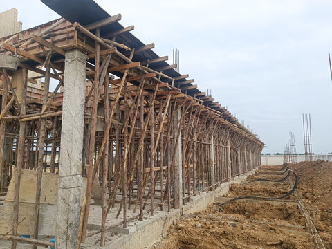 Construction site with timber scaffolding and concrete columns under development, showing early stages of commercial or residential building structure. Wooden framework supports