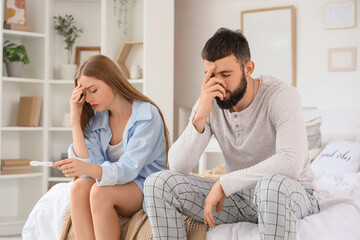 Upset young couple with pregnancy test sitting in bedroom