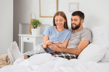 Happy young couple with pregnancy test lying in bedroom