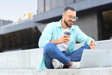 Young man with laptop video chatting outdoors