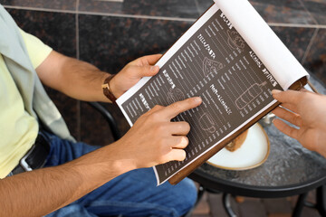 Fototapeta premium Young man with menu and waitress ordering drink in street cafe, closeup