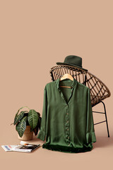 Obraz premium Hanger with stylish female blouse hanging on armchair, hat, houseplant and magazines against color background