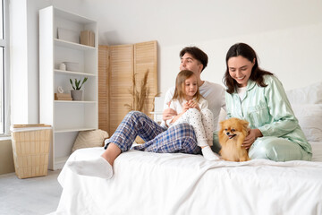 Happy little girl with her parents and Pomeranian dog sitting in bedroom