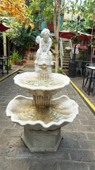 statue of the angel of love, namely cupid, as a garden decoration with details of a two-story fountain with a shell pattern, made of rough white stone as a symbol of good luck