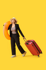 Young businesswoman with swim ring and suitcase waiting for summer vacation on yellow background