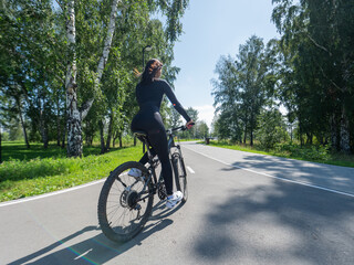 Fototapeta premium Rear view of Caucasian woman riding bike in park. 