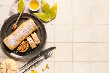 Plate with tasty pumpkin strudel, seeds and bowl of honey on white tile background