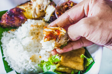 People enjoy grilled chicken rice with spicy chili sauce and vegetables using their hands or Fingerfood or muluk. A noble tradition of Javanese culture
