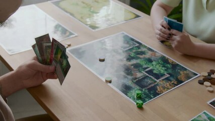 Close up view of hands of unrecognizable man throwing dice, showing card and making move on illustrated map while playing tabletop game with girlfriend at home - Powered by Adobe