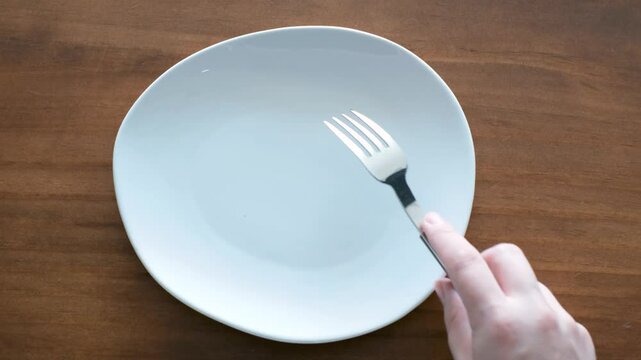 Female hands holding a fork and knife next to an empty plate on wooden background close-up top view.