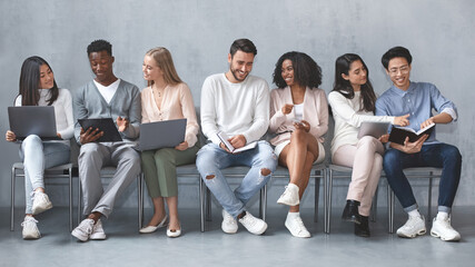 Group of multiracial young people waiting for job interview, talking to each other and smiling