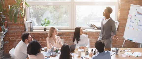 Black guy with digital tablet sharing his business ideas with international colleagues during...
