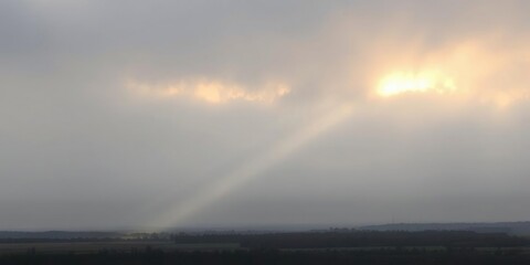 Obraz premium A lone sunbeam breaks through the dense layer of grey clouds, casting a warm glow on the landscape below, nature, weather