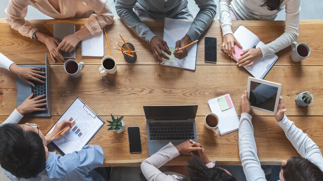 Office lifestyle concept. Top view of international young business team having meeting at office, sitting around table