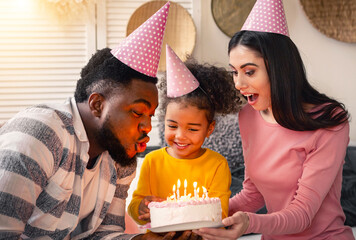 African american father and european mother help daughter blow out candles on the cake